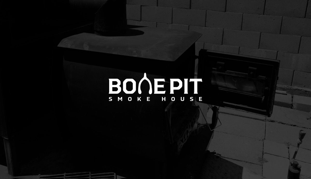 The Bone Pit Smoke House wordmark, its N drawn as a wishbone, reversed in white over a photograph of the smoker.