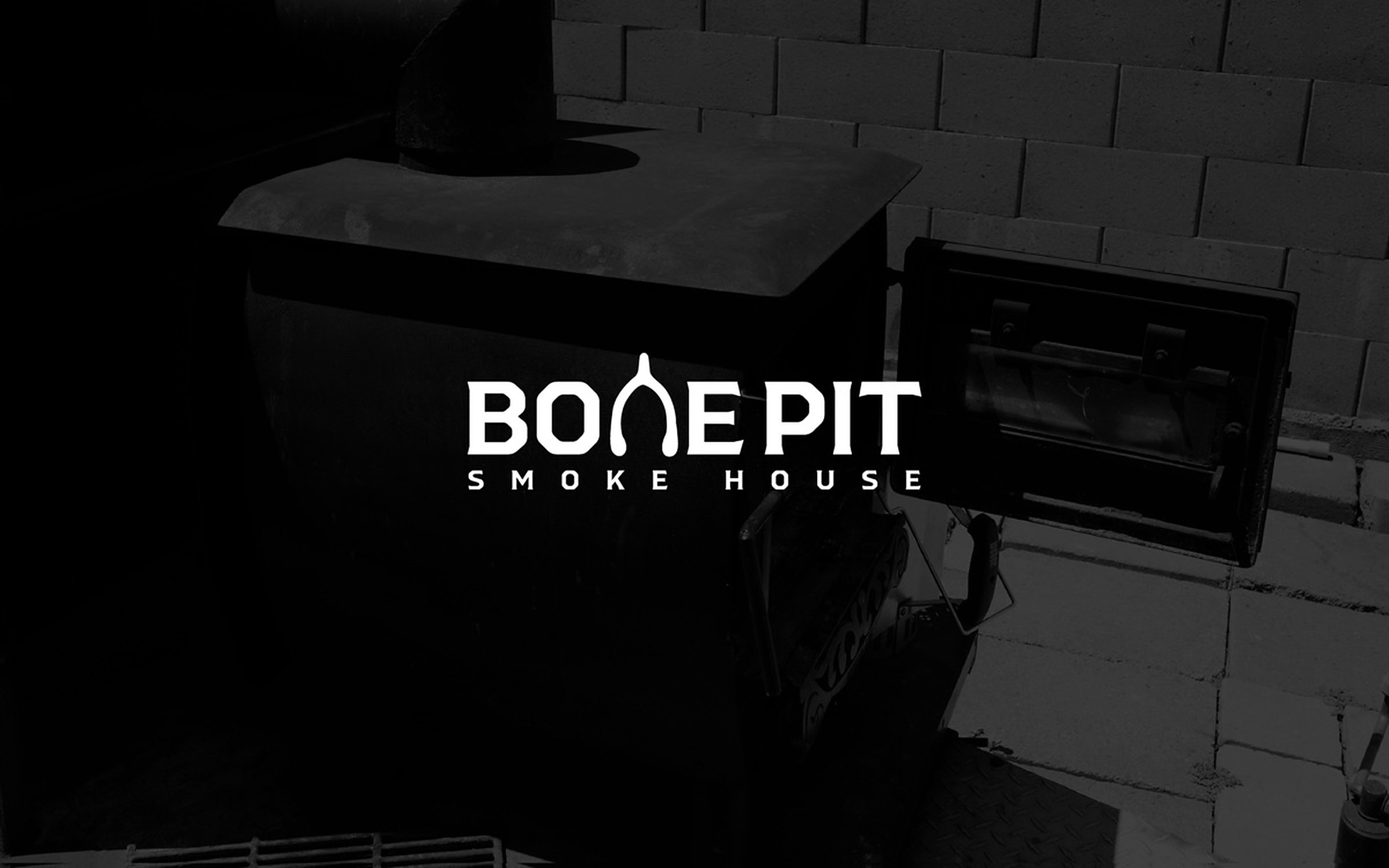 The Bone Pit Smoke House wordmark, its N drawn as a wishbone, reversed in white over a photograph of the smoker.